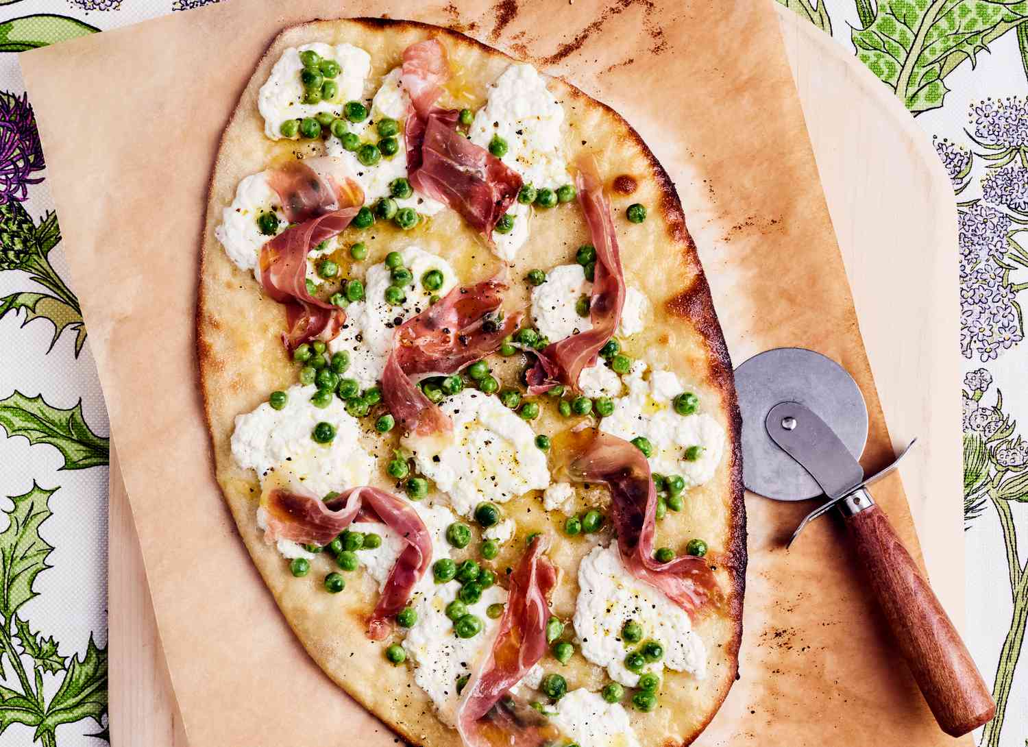 overhead view of a thin crust pizza with ricotta, prosciutto and peas