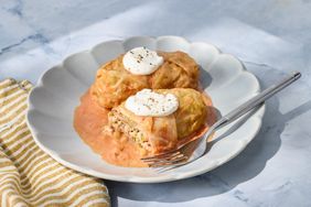 Two stuffed cabbage rolls on a plate with sauce and dollops of cream accompanied by a fork on a striped napkin