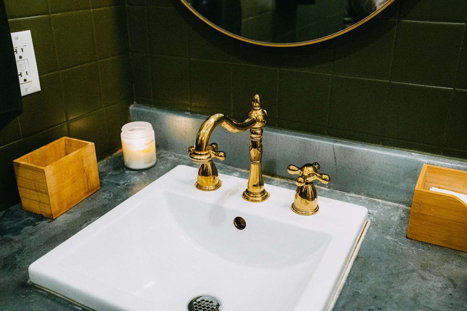 Bathroom sink with a brass faucet candle and wooden containers on a gray countertop
