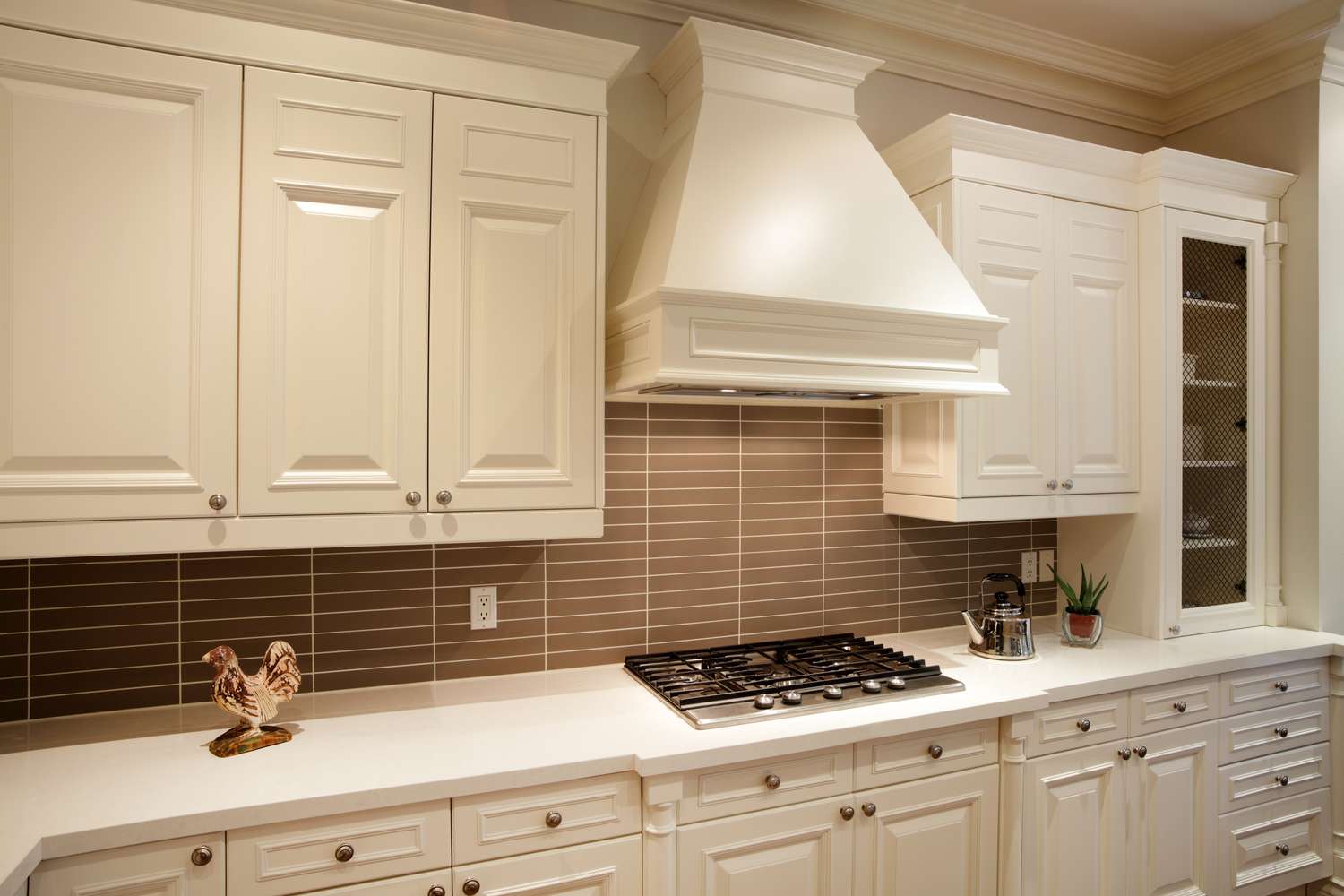 Modern kitchen featuring cabinets an exhaust hood and a stovetop with utensils and decor on the counter