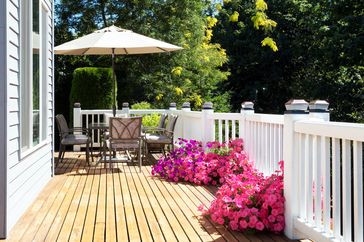 A wooden deck with patio furniture umbrella and pink flowers along the railing