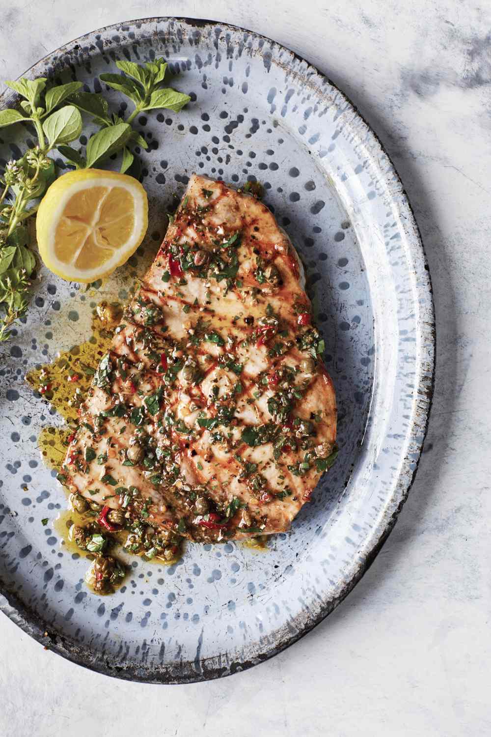 swordfish with sicilian oregano-caper sauce served on a blue speckled plate