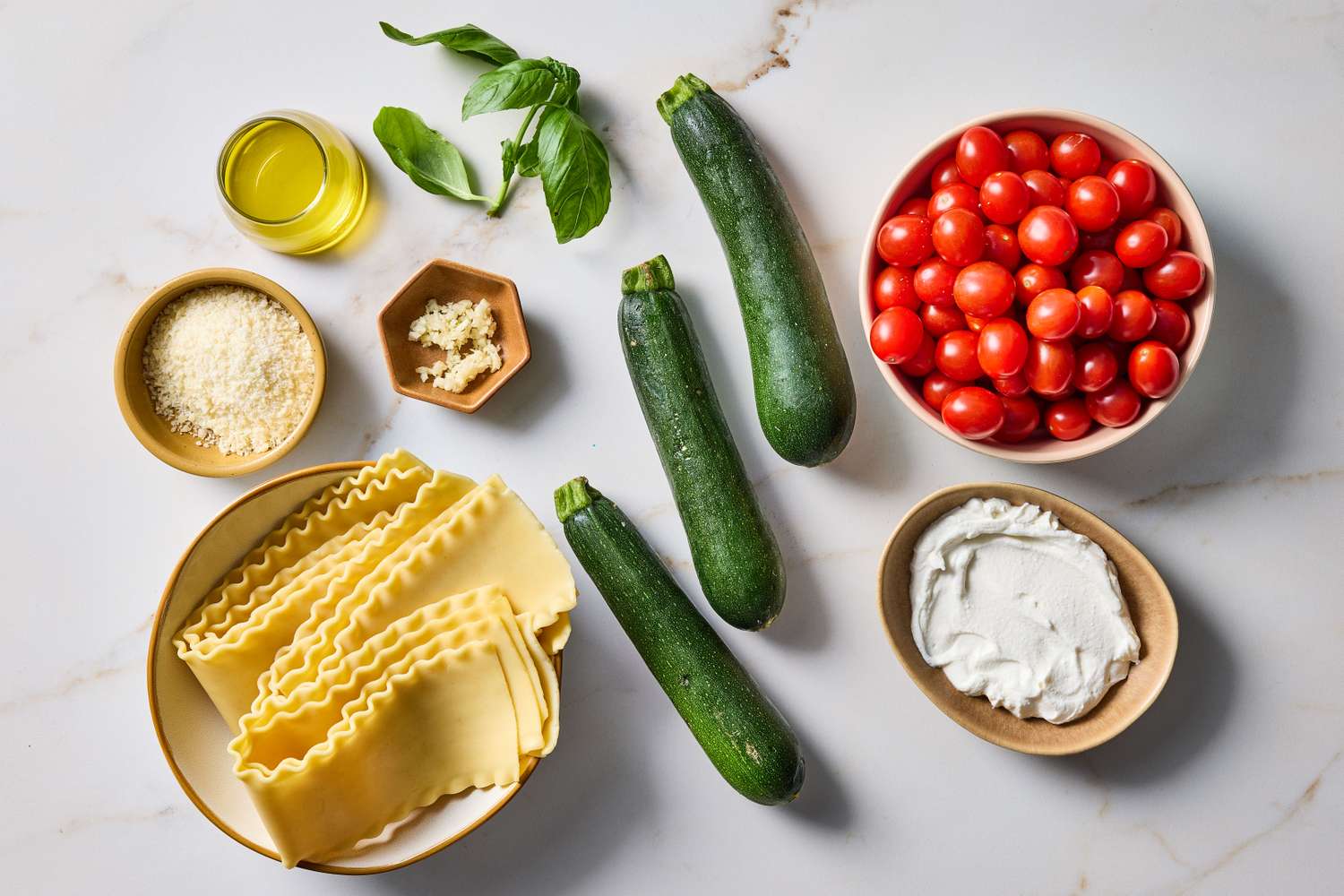 Lasagna noodles zucchini cherry tomatoes ricotta grated cheese olive oil basil leaves and garlic arranged on a surface