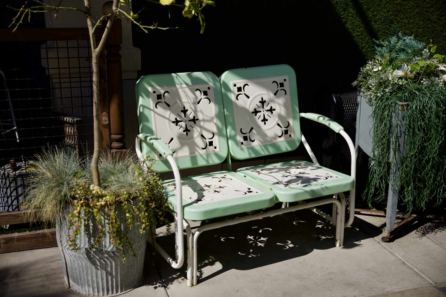 A metal bench with decorative cutouts is positioned outdoors near potted plants on a patio