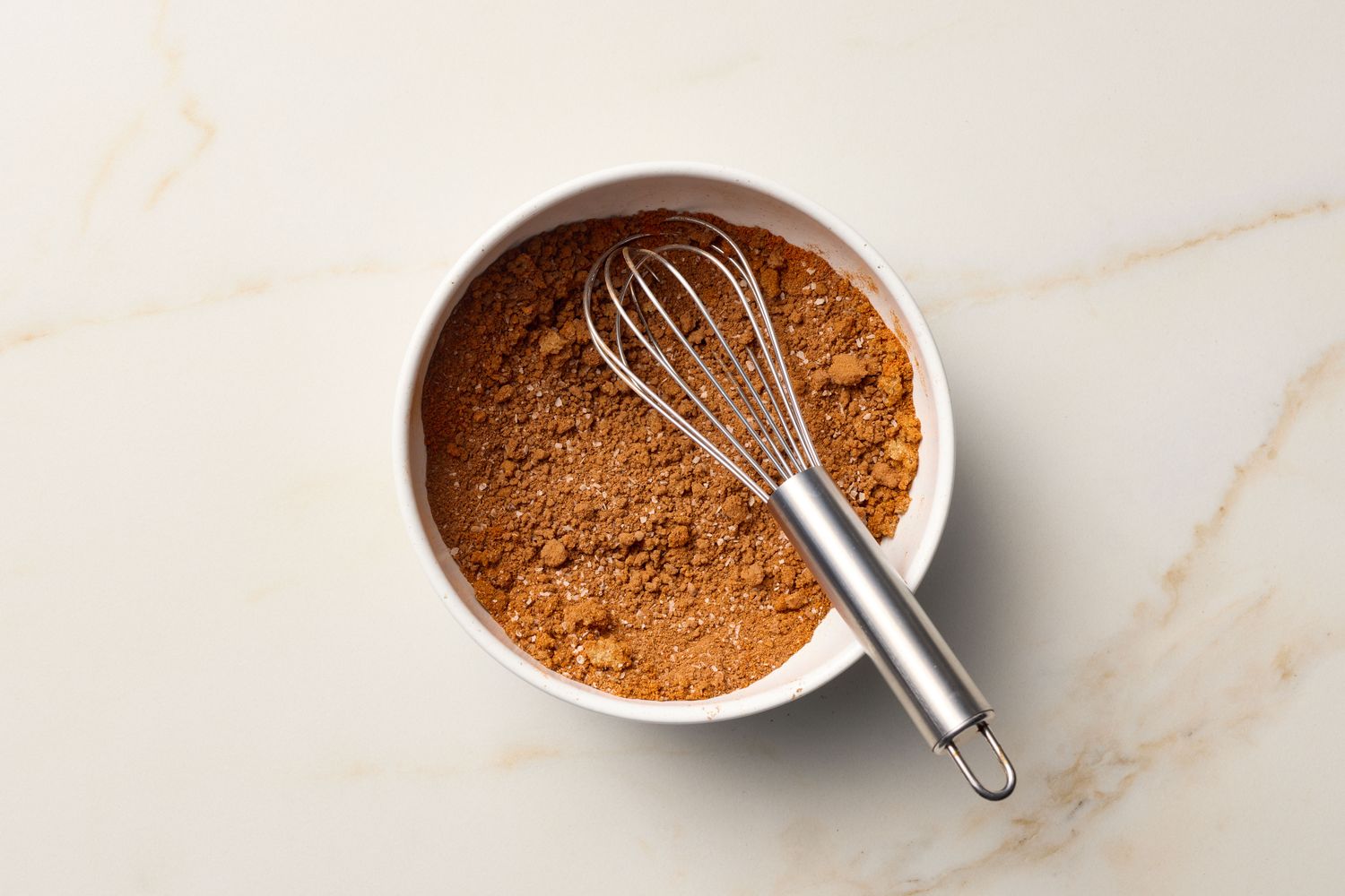 A bowl of dry seasoning mix with a whisk on a light marbled surface
