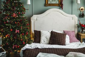 Bedroom interior decorated for Christmas with light green walls, double bed and green Christmas tree decorated with red ornaments and lights. Cozy bedroom for holidays in boutiqe hotel.
