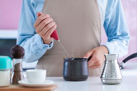 woman using a milk frother in a black ceramic vessel