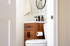 A small bathroom with a wooden vanity cabinet a round mirror and a toilet