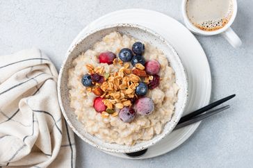 Breakfast bowl of porridge topped with berries and granola beside a cup of coffee and a napkin