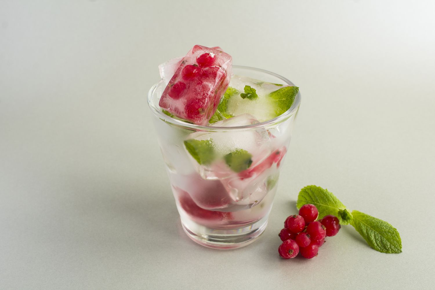 Ice with frozen berry and mint in the drinking glass on the gray background