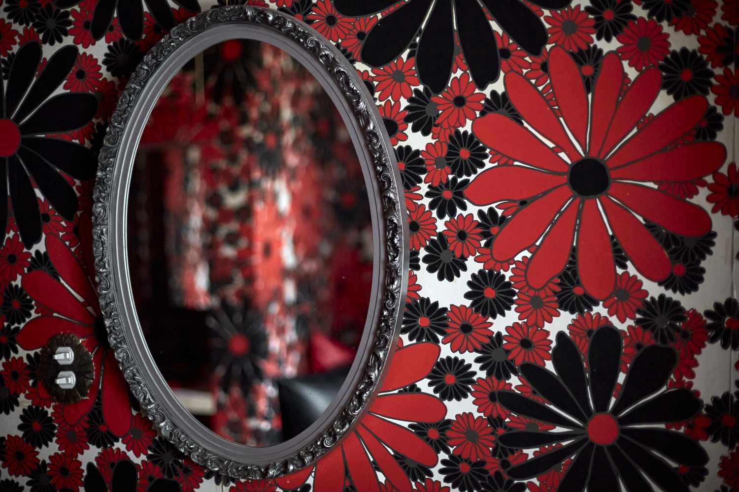 An oval mirror is mounted on a floral patterned wall reflecting part of the same wall design