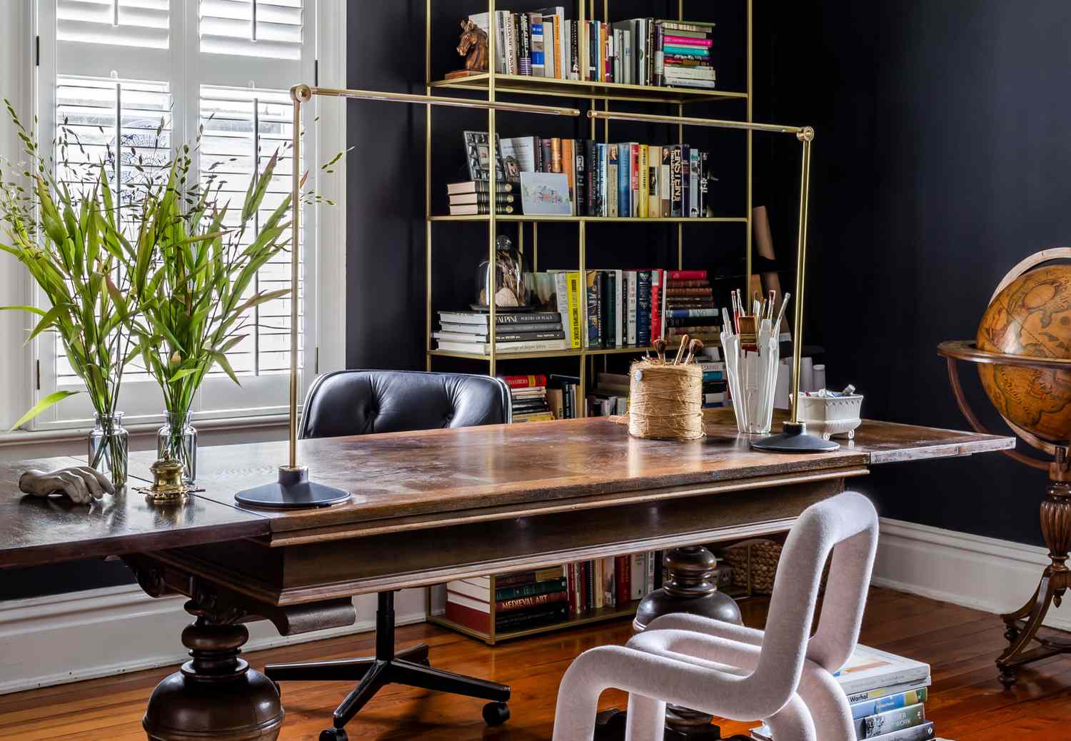 A study room featuring a wooden desk bookshelves stacked with books and a globe in the corner a chair positioned by the desk