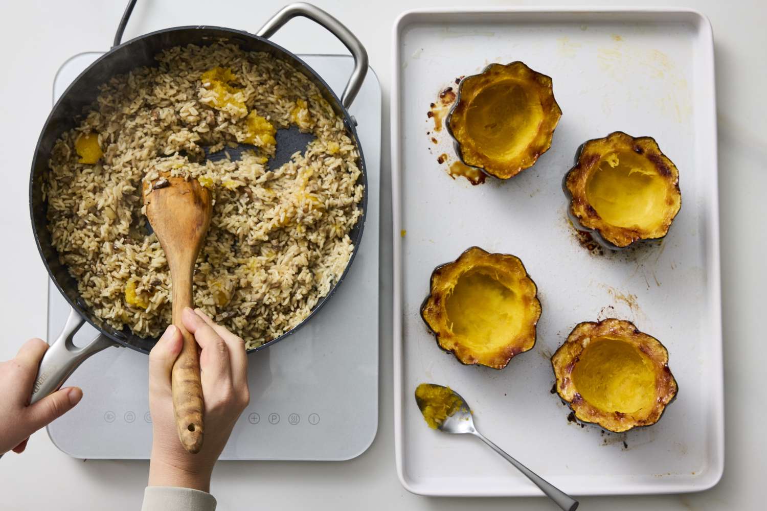 A person stirring a skillet of rice and filling roasted acorn squash halves on a tray