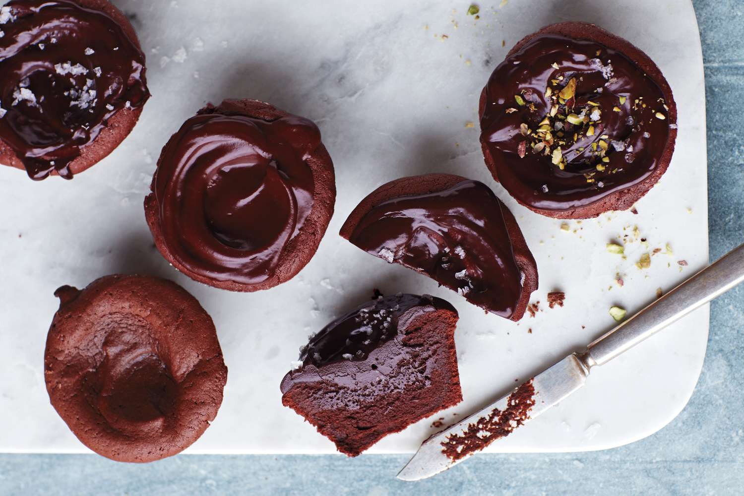 Collection of molten chocolate cupcakes on a cutting board some topped with frosting and garnishes one is cut open to reveal the inside