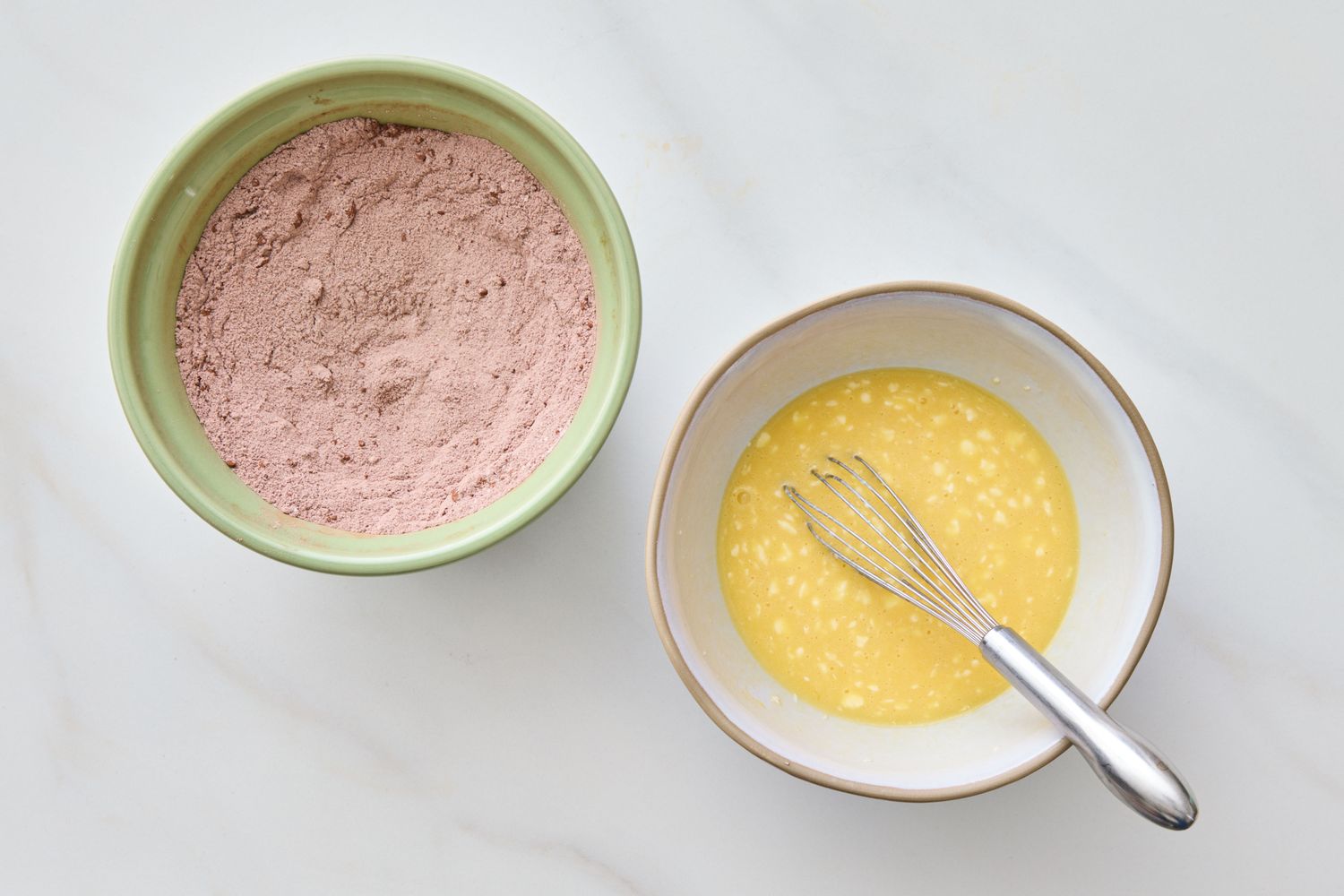 Two bowls one with dry cake mix and the other with a whisk in wet ingredients on a countertop