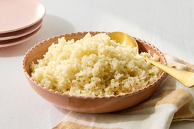 A bowl of Arborio rice with a gold spoon displayed on a table with a napkin and plates