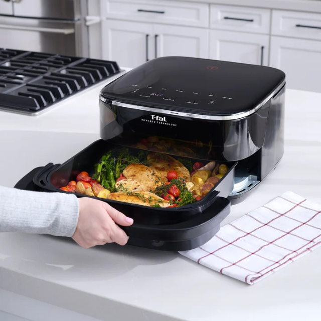 A Tfal appliance with a tray of cooked vegetables and chicken on a kitchen countertop