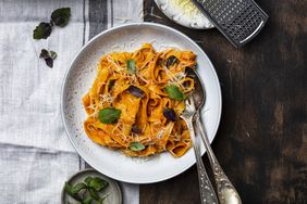 A plate of pasta garnished with herbs and accompanied by a grater and a small bowl of leaves