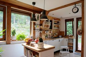 A cozy kitchen with wooden accents, a central island, and large windows overlooking greenery, shelves holding kitchen accessories