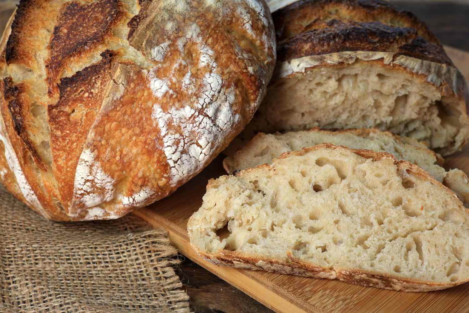 Loaf of artisanal bread with slices revealing airy texture on a cutting board