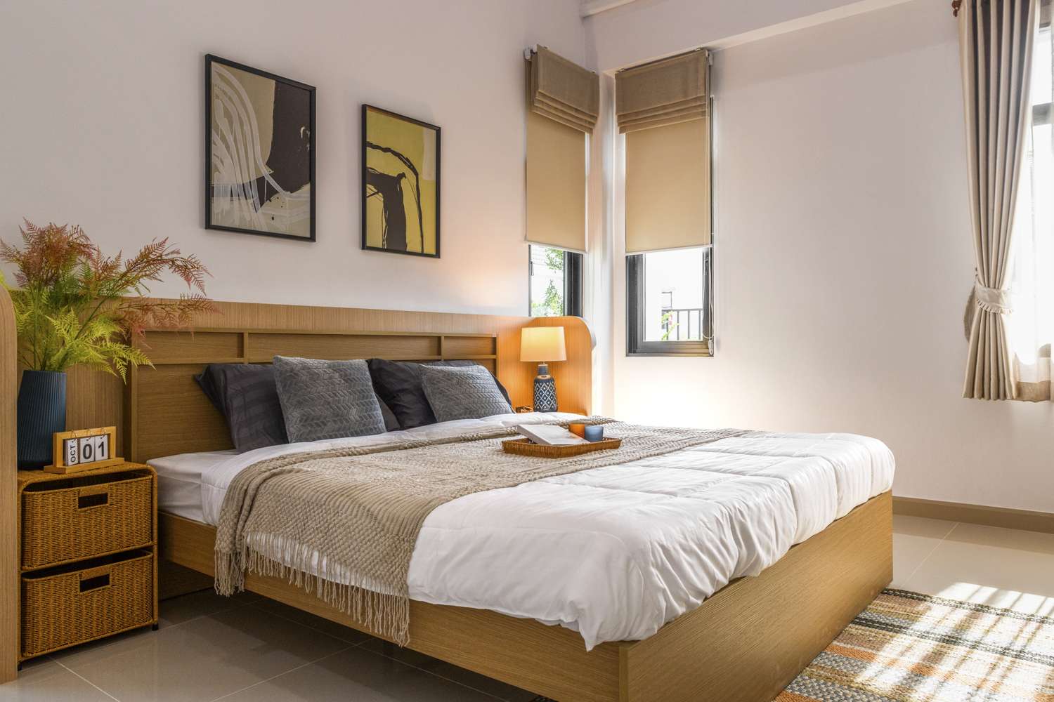 A neatly arranged bedroom with furniture artwork on the wall and a bed with cushions and covers