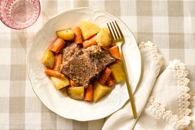 Plate with pot roast carrots and potatoes placed on a checkered tablecloth