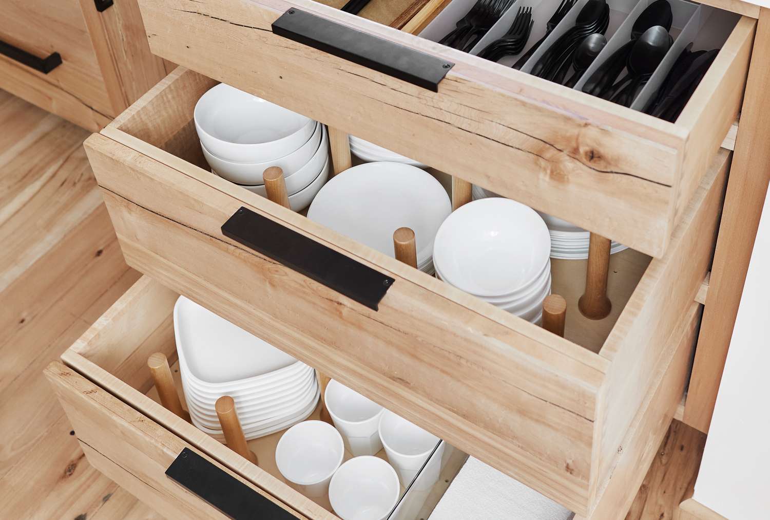 Open wooden kitchen drawers organized with plates bowls cups and utensils