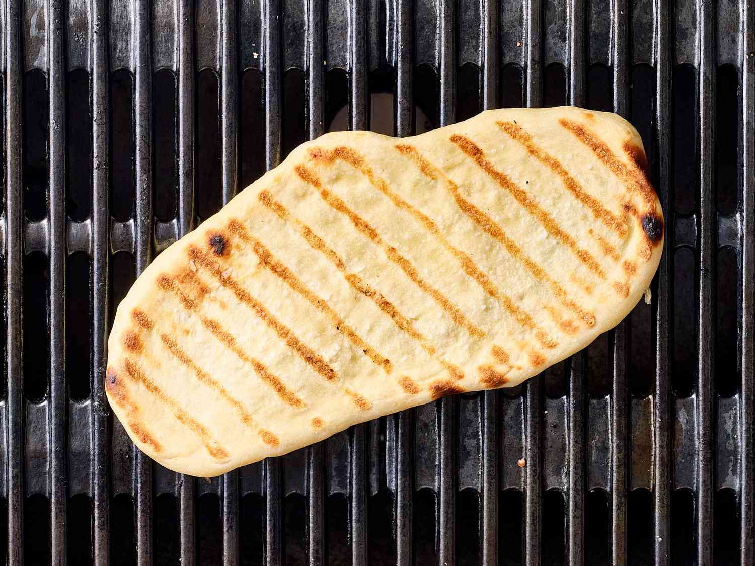 Grilled pizza dough on a grill grate