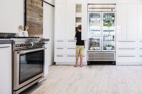 A modern kitchen with a person standing near the refrigerator accessing a cabinet