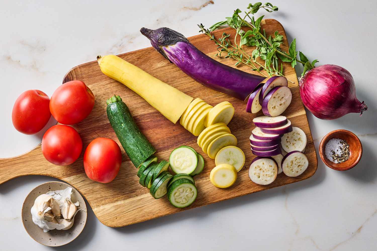 Sliced vegetables and ingredients on a wooden board including tomatoes zucchini eggplant and garlic preparation for a dish
