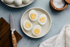 A plate containing four halved hardboiled eggs a knife and cloth napkin nearby