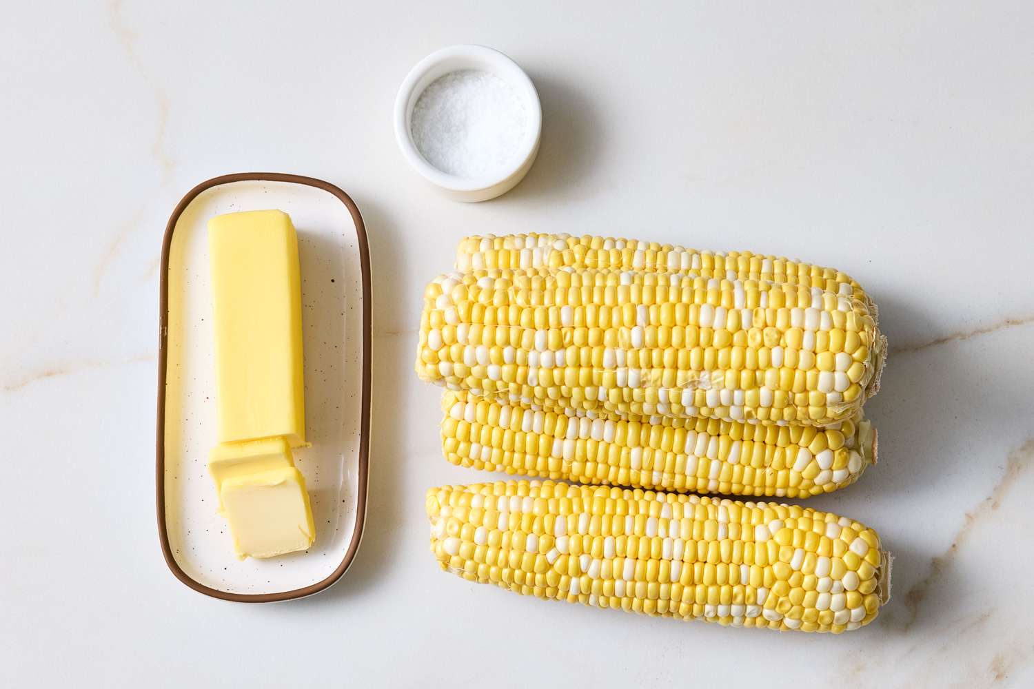Three ears of corn with a stick of butter and a small dish of salt