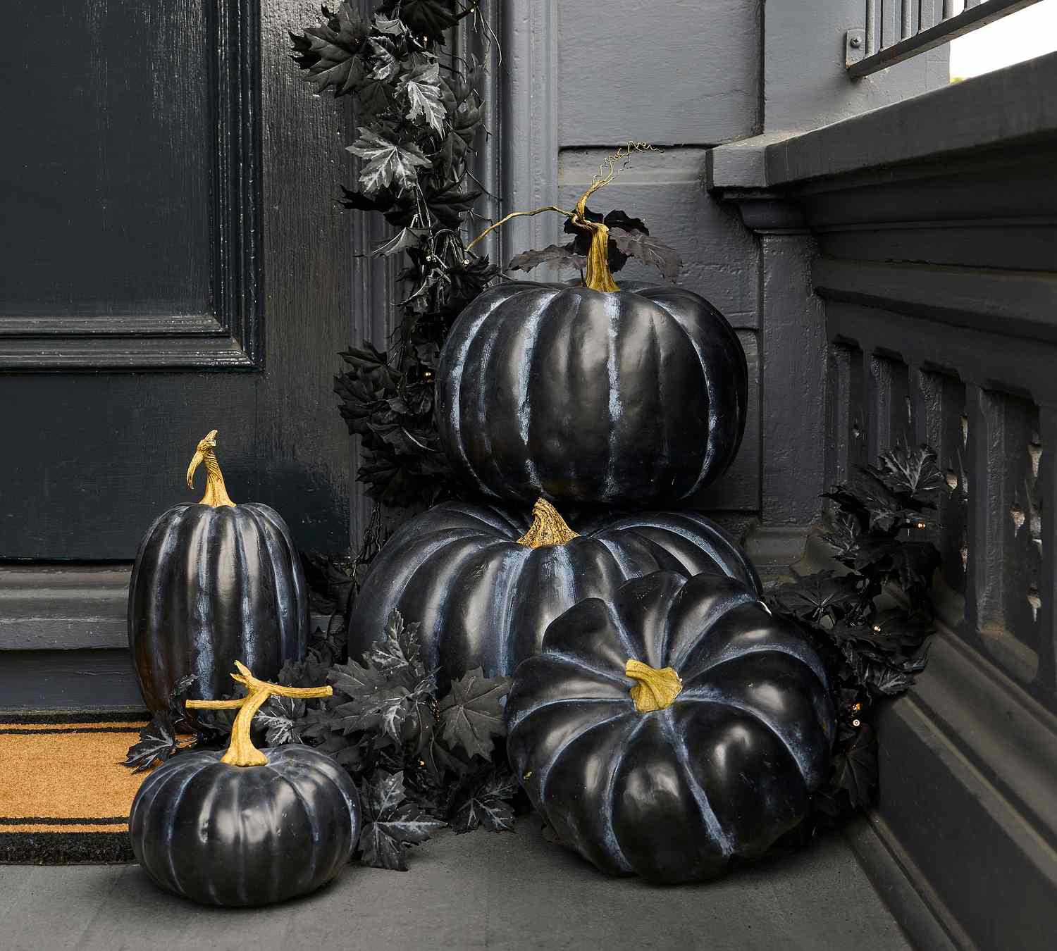 Black pumpkins arranged on a doorstep with decorative leaves
