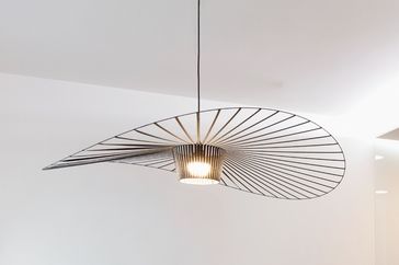 A modern ceiling light with a linear wave design suspended in a minimalist room