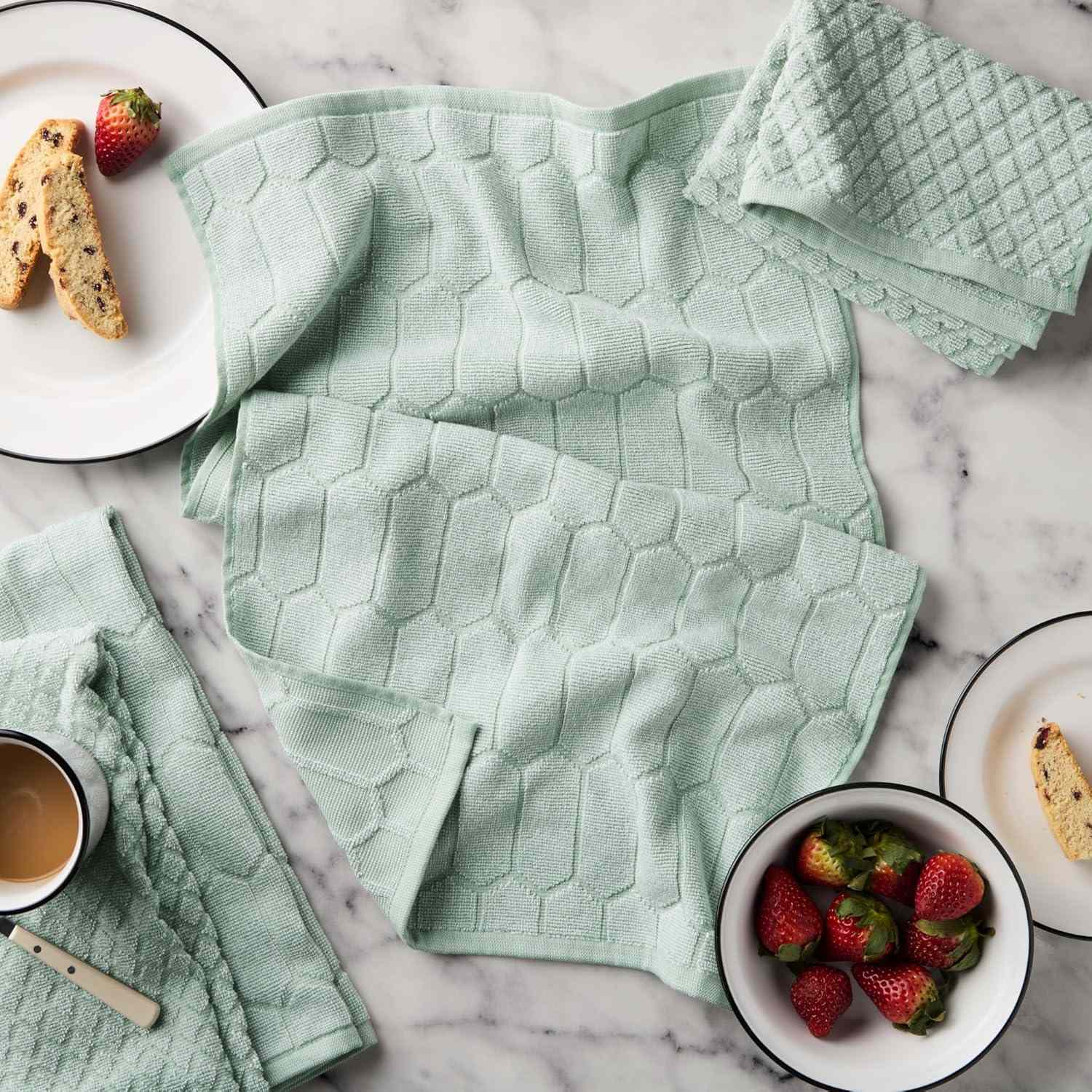 Textured kitchen towels laid on a table with dishes containing strawberries and biscotti