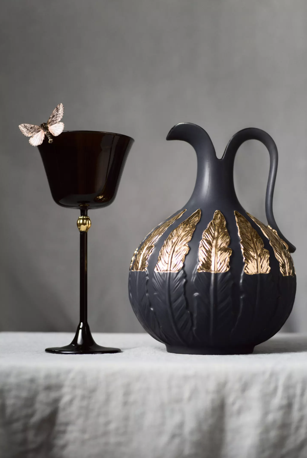 A black decorative pitcher with gold leaf accents and a matching goblet on a surface