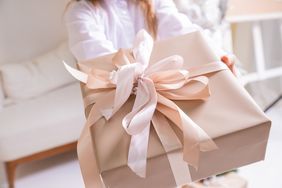Hands presenting a gift wrapped in decorative paper with a bow