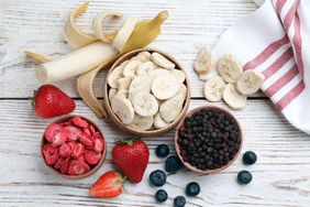 Assorted fresh and freezedried fruits including strawberries blueberries and bananas on a wooden surface