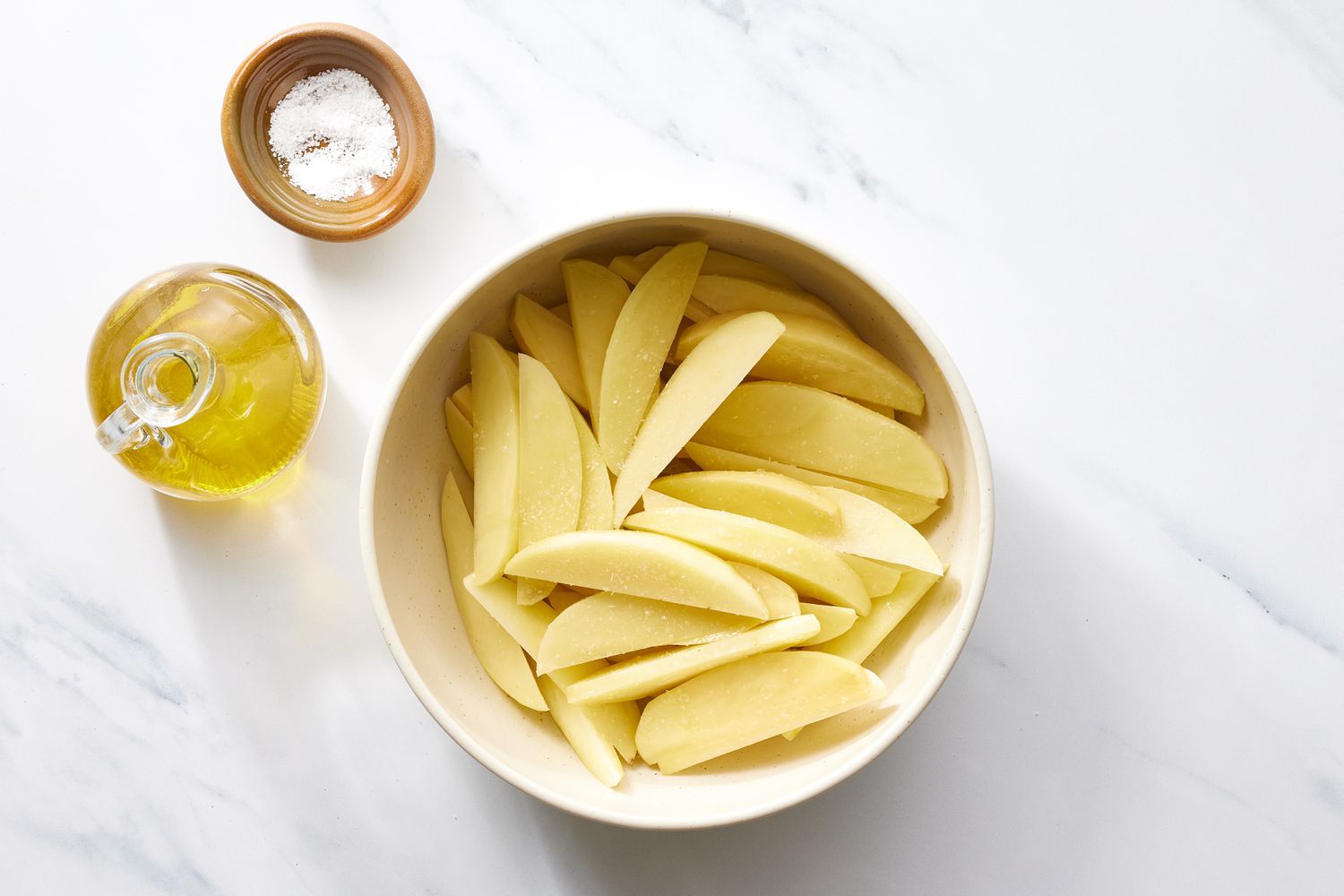 Potato wedges in bowl with oil and salt 
