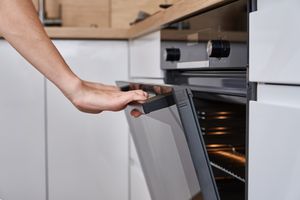 A person opening a modern oven in a kitchen environment