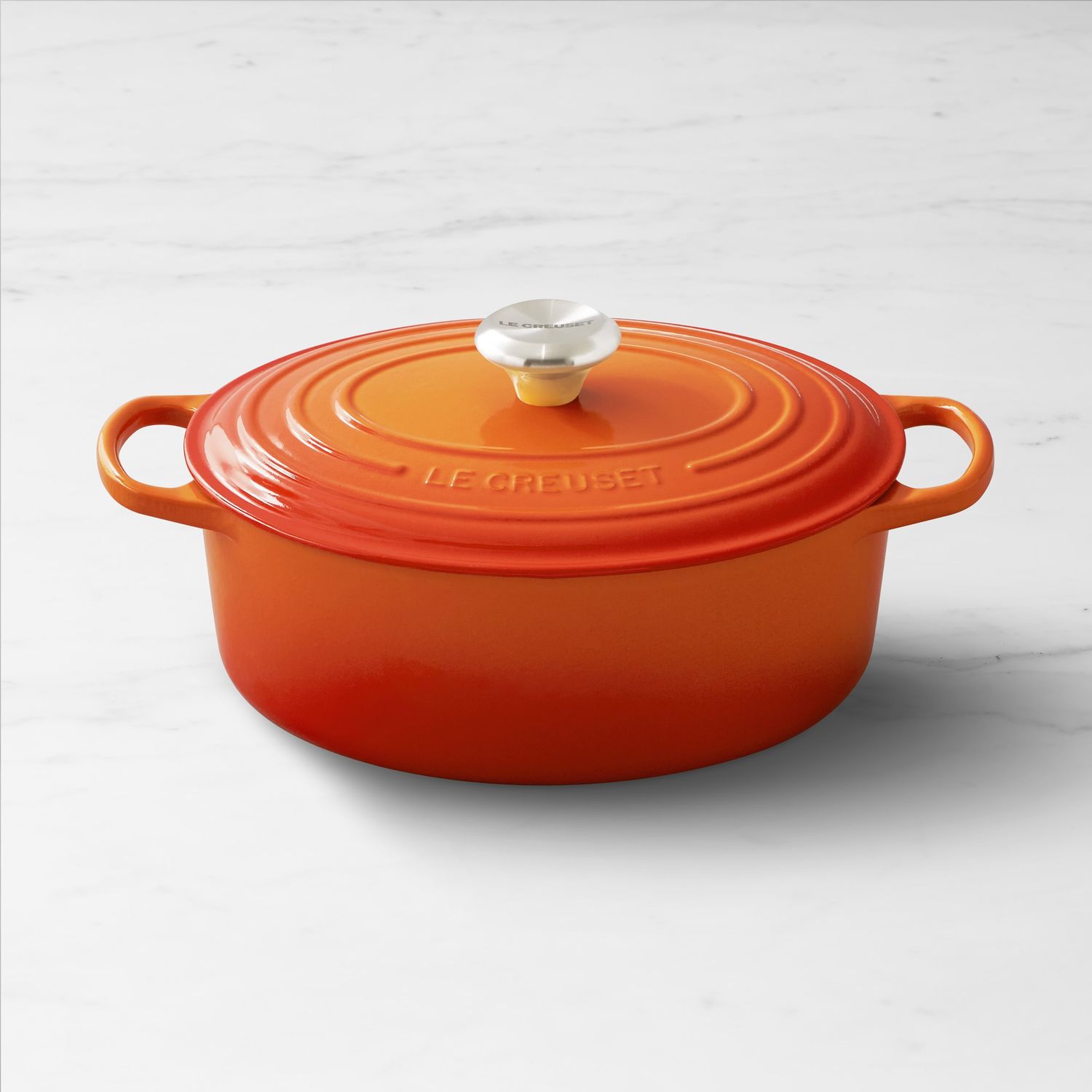 A lidded castiron dutch oven featuring two handles and a metallic knob resting on a white surface