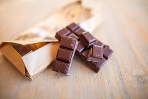 A pile of chocolate squares spilling out of a brown paper wrapper on a wooden surface