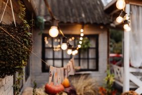 Outdoor holiday lights strung up in front of a wooden house with visible decorations like pumpkins and seasonal foliage