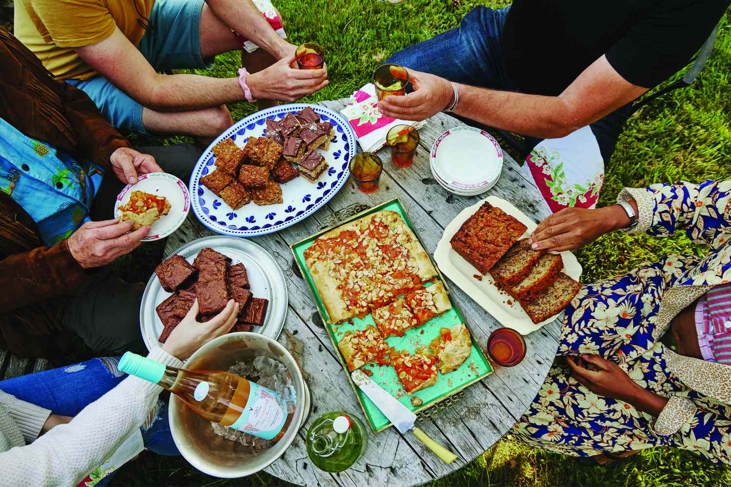 people around an outdoor table with several desserts on it