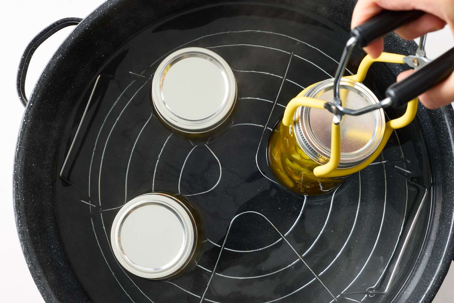 Using a jar lifter to place a jar of pickles into or remove it from a canning pot filled with water