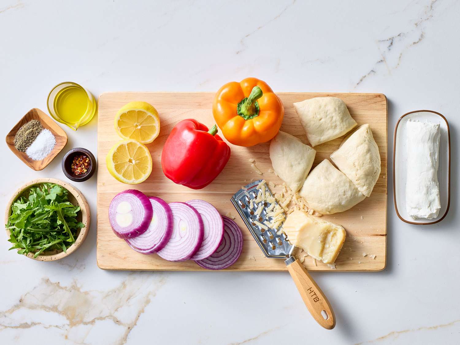Ingredients for a grilled pizza, including bell peppers, red onions, pizza dough, and cheese on a cutting board