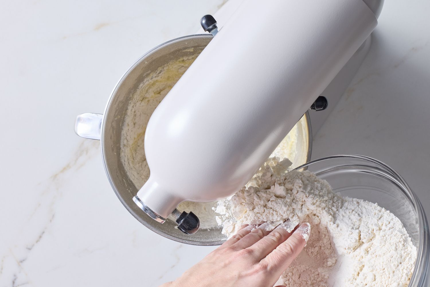Bowl of flour being added to a stand mixer with creamy batter
