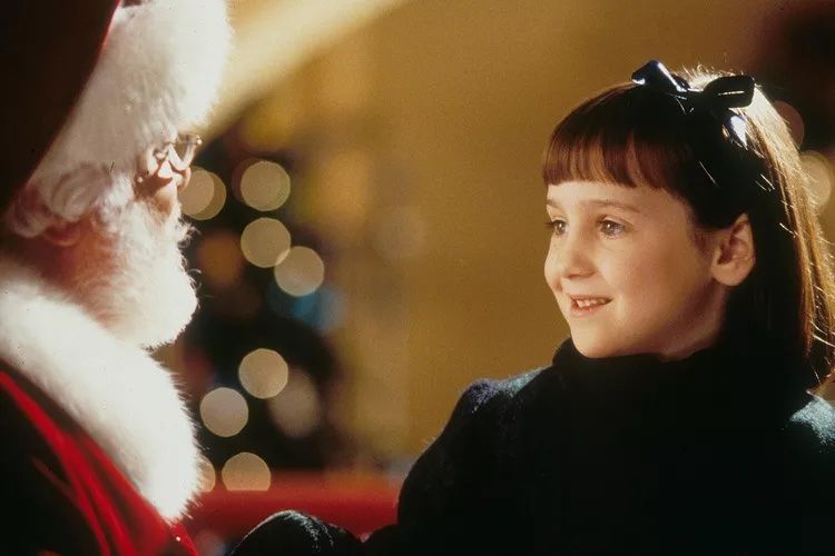 Mara Wilson smiling interacting with a person in a Santa costume