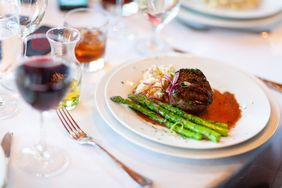 A plated meal featuring steak asparagus and mashed potatoes served with a glass of red wine on a dining table