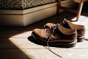 A pair of leather dress shoes on a wooden floor near a corner of a room with floral wallpaper